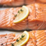 Perfectly cooked salmon fillets on a plate with lemon and herbs